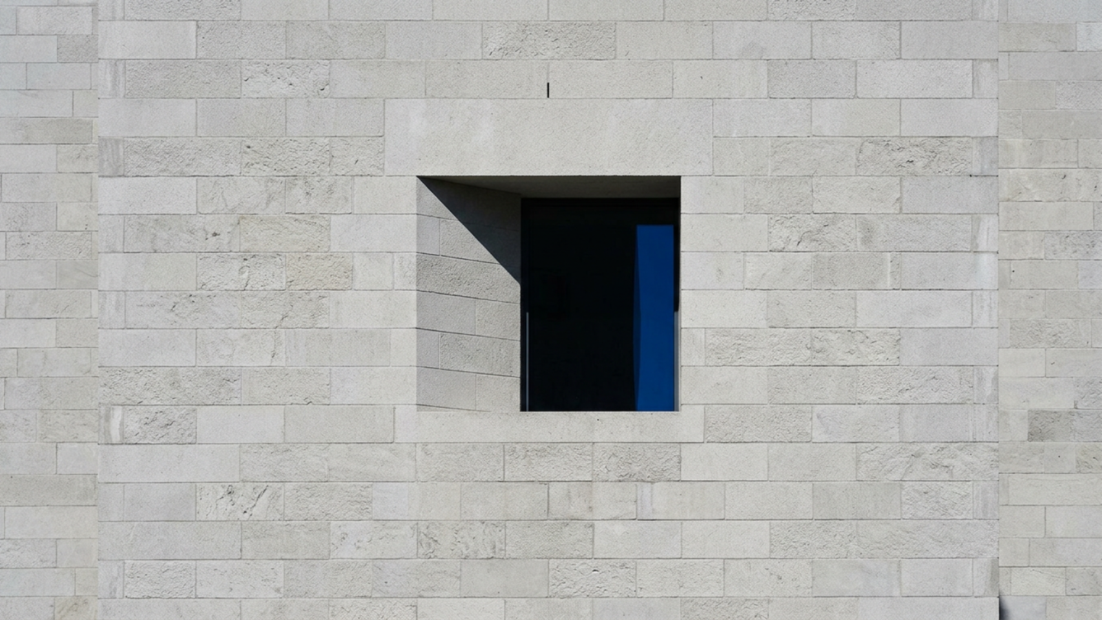 A close-up of a high-mass concrete facade with deeply recessed square windows casting sharp shadows.
